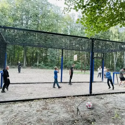 Mieszkańcy grają w zamkniętym mini boisku Football Box zamontowanym na polanie parku - realizacja w otoczeniu przyrody.