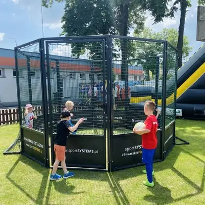 Dzieci bawią się w arenie Football Octagon podczas festynu rodzinnego - mobilna atrakcja piłkarska dla najmłodszych.