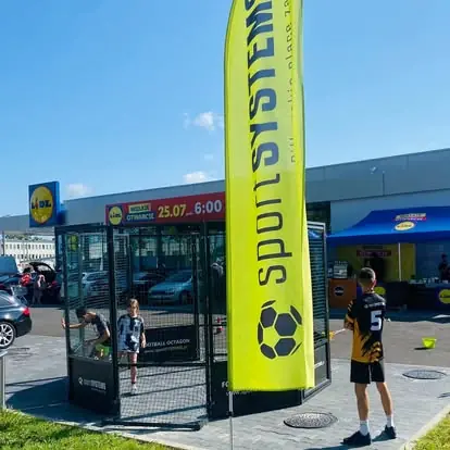 Football Octagon z flagą reklamową w strefie atrakcji eventu plenerowego przy centrum handlowym.