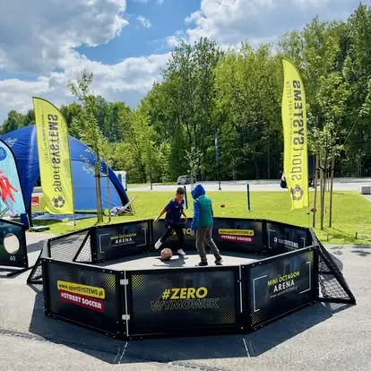 Dzieci grają w Mini Octagon Arena w strefie Street Soccer podczas eventu plenerowego.